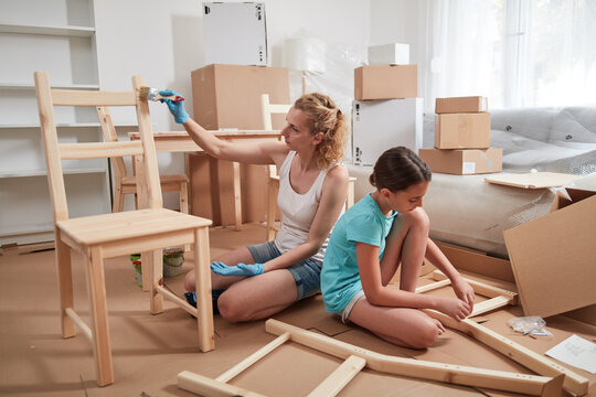 Mother and daughter painting and assembling furniture in new apartment, moving in and being hardworking.