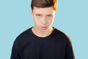 Sullen guy. Teen anger. Bullying violence. Portrait of dissatisfied insecure offended boy in black t-shirt looking at camera isolated on blue copy space background.