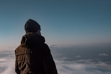 Man in a jacket in the mountains. The guy dreams and looks into the distance.