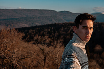 Naklejka na ściany i meble Young man in a sweater against the background of mountains. Autumn landscape. The guy is a traveler.