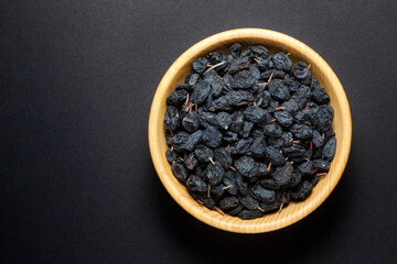 Black currant raisins in a wooden bowl on black background. Top view.