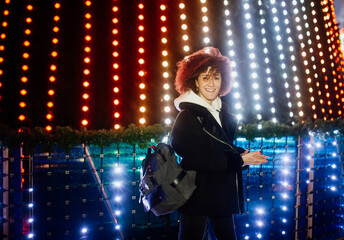 Curly girl with the backpack walks in the night city on a festive night.