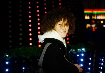 Curly woman against the background of a city Christmas tree decorated with lights.
