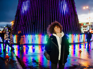 Young woman with curly hair against the background of glowing Christmas lights.