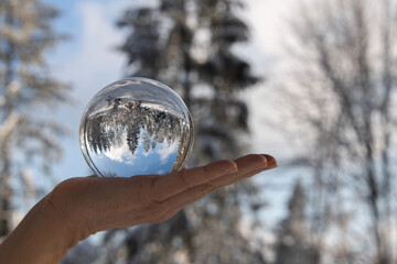verschneiter Wald spiegelt sich in Glaskugel, die in der Hand gehalten wird, Naturerlebnis im...