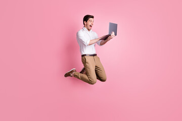 Full length photo portrait of screaming guy jumping up holding laptop isolated on pastel pink...