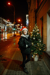 The portrait of a young girl outside in the evening dressing winter clothes and a Christmas Santa holiday hat