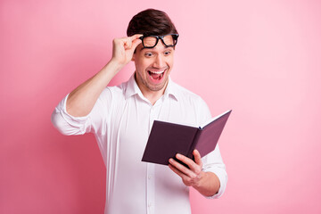 Portrait of optimistic guy hold book take off spectacles wear white shirt isolated on pink color background