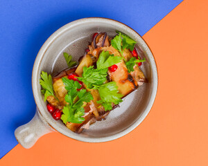 Egg-plant rolls with meat and pomegranate seeds served in a bowl over orange and blue background.