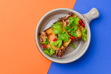 Egg-plant rolls with meat and pomegranate seeds served in a bowl over orange and blue background.