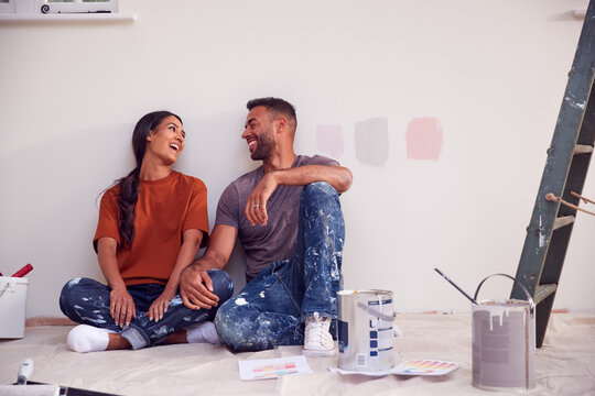 Couple Taking A Break From Painting Test Squares On Wall As They Decorate Room In New Home Together