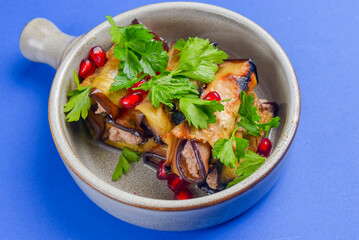 Egg-plant rolls with meat and pomegranate seeds served in a bowl over blue background.