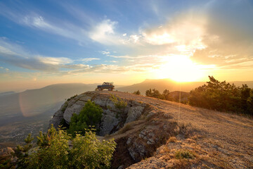 Jeep near a steep cliff against the background of mountains and the setting sun in the blue sky