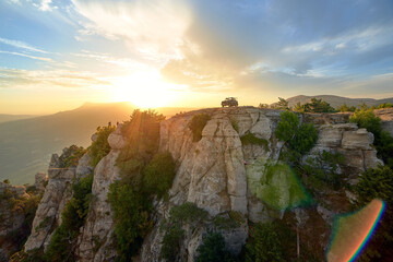 Jeep near a steep cliff against the background of mountains and the setting sun in the blue sky
