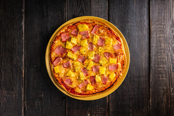 Just baked hawaiian pizza with freshly chopped pineapple and ham on the rustic wooden background. Selective focus.