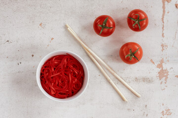 Fototapeta na wymiar the texture on the surface of the red noodles in a bowl, ripe tomatoes and chopsticks