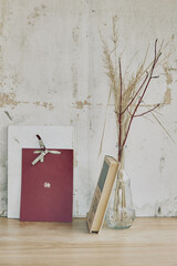 still life in the form of a glass transparent vase with dried grass and books on the background of a vintage wall