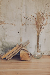 still life in the form of a glass transparent vase with dried grass and books on the background of a vintage wall