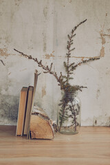still life in the form of a glass transparent vase with dried grass and books on the background of a vintage wall