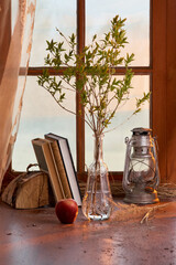 spring twig in a transparent glass vase with a kerosene lamp and books on the background of the window