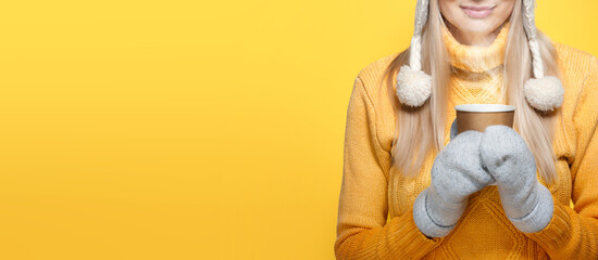 poster, a positive cheerful woman in a yellow sweater, white hat and light mittens holds a paper mug with a hot drink.