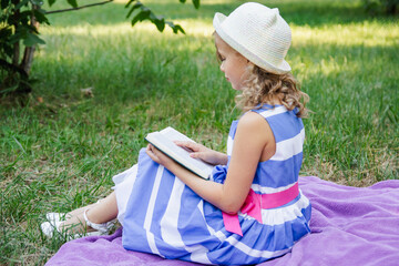 little happy girl in a dress in the park on the grass reads a book