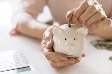 Hands of old women's put money coins in a piggy Bank, the concept of retirement.