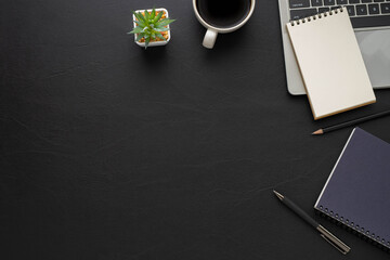 Top view above of Black leather office desk table with keyboard, notebook and coffee cup with...