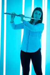 Portrait of a professional flute player playing a wind instrument. Young woman posing in a dark studio against the backdrop of bright neon lights.