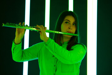 Woman in a white blouse plays the flute against a background of bright neon lights. Cute young female artist with a musical instrument in his hands. Poster for advertising a music school. Close up. © kinomaster