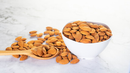 Almonds in white porcelain bowl with wooden spoon on the table.Healthy food Concept.