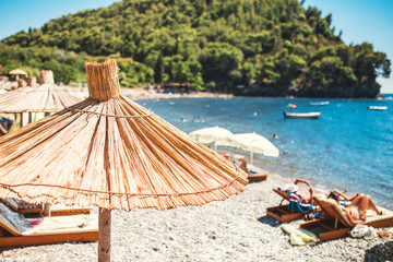 Fototapeta na wymiar Sunny beach in the lagoon with a sun umbrella in the foreground - tourist season in a seaside resort