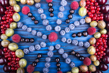 Ornament of assorted fruits and berries: gooseberries, raspberry, red and black currant, blueberry, sweet cherry. Blue wooden background.