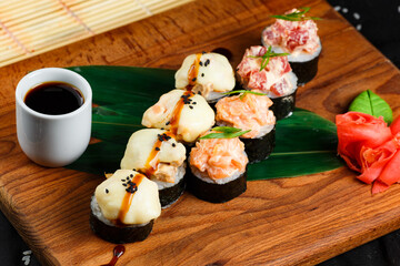 japanese sushi rolls with cheese cap and roll with raw salmon and tuna in a restaurant serving on a wooden board on a dark background. top view.