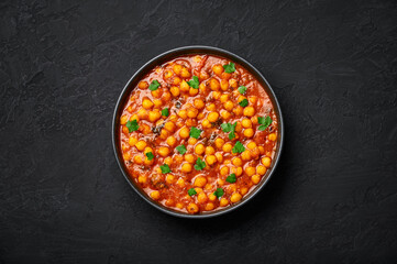 Chana Masala or Chole in black bowl on dark slate table top. Indian cuisine veg chickpeas curry dish. Asian spicy vegetarian food and meal. Top view