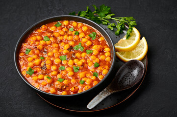 Chana Masala or Chole in black bowl on dark slate table top. Indian cuisine veg chickpeas curry...