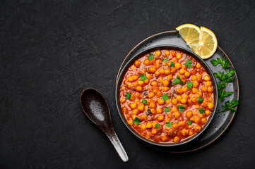 Chana Masala or Chole in black bowl on dark slate table top. Indian cuisine veg chickpeas curry dish. Asian spicy vegetarian food and meal. Copy space. Top view