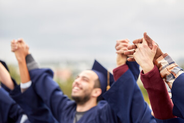 education, graduation and people concept - group of happy international students in mortar boards and bachelor gowns holding hands and celebrating success