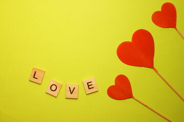 Three red hearts on a yellow background. The word love. View from above. Hearts are on the right....