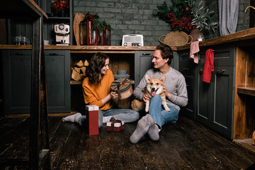 Obraz na płótnie Canvas Happy caucasian couple on the kitchen floor with their corgi dog. Young family, woman and man giving each other gifts. Valentines day