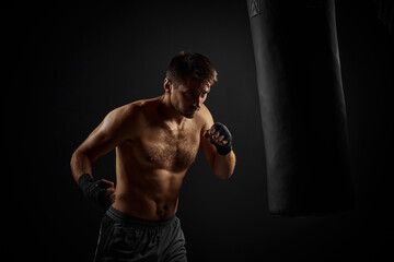 Fototapeta na wymiar Male boxer punching in boxing bag on black background