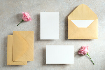 Wedding invitation cards and stationery top view. Flat lay blank paper card, kraft paper envelopes, flowers on stone table. Vintage style.
