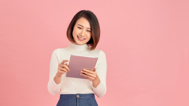 Young beautiful woman using smartphone gadget ipad.Lifestyle concept. Isolated on pink background.