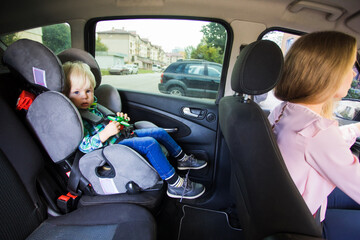 The little boy is sitting in a car seat rides with his mom