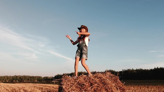 Rural girl child dancing on a bale of straw on a Sunny summer evening against a blue sky background. Slow motion