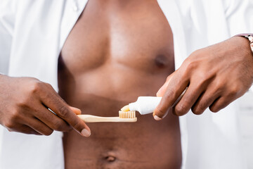 Cropped view of african american man squeezing toothpaste on toothbrush on blurred background