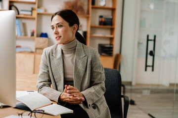 Pleased charming woman working with computer and planner in office