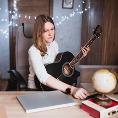 Fototapeta na wymiar Blonde caucasian girl remotely learns to play the guitar - online music tutor training