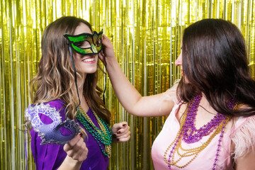 Mardi gras party. Two women with a carnival mask and beads on the golden festive background