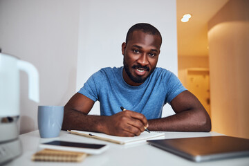 Mixed-race freelancer is writing in a kitchen